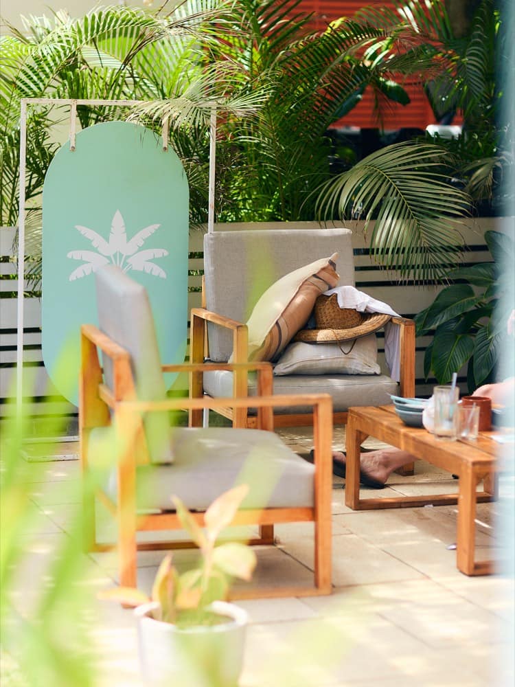Rincón lounge de Baya Baya con palmas, cojines y el panel de la palmera de marca
